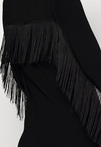 Vêtement noir avec une coupe ajustée, comprenant des côtes verticales et un détail à franges à l'arrière, fabriqué dans un tissu lisse.