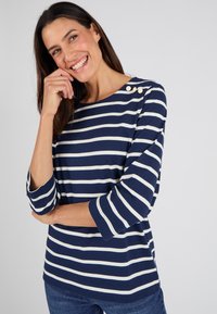 Maglietta a righe blu navy e bianca a maniche lunghe, con scollatura rotonda e maniche a tre quarti, caratterizzata da dettagli con bottoni sulla spalla.