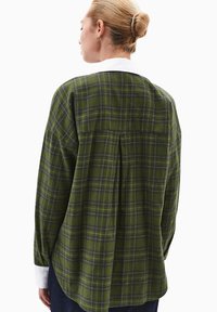 Camicia a quadri verdi in flanella con colletto bianco, dotata di una schiena plissettata e maniche lunghe, vista dal retro.