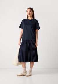 Navy T-shirt with short sleeves and round neckline, paired with a pleated navy skirt. White sneakers, light beige socks, and a cream tote bag.
