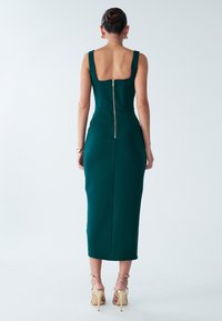 Groene midi-jurk met een getailleerd ontwerp, brede bandjes en een ritssluiting aan de achterkant. Gecombineerd met beige, gestripte hoge hakken. Soepele textuur.