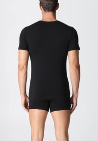 T-shirt nera aderente a maniche corte con texture liscia, scollo rotondo e cuciture visibili. Indossata con pantaloni corti neri abbinati.