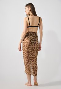 Jupe transparente imprimée léopard dans des tons marron, longueur cheville, avec une texture lisse et un tombé subtil, portée sur un haut noir.