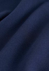 Tessuto blu navy con una texture liscia, caratterizzato da motivi sottili e un aspetto leggermente drappeggiato. Il materiale è leggero e flessibile.