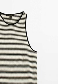 Stibet ærmeløs tanktop i creme og sort, med ribbet tekstur og en rund halsudskæring med kontrastkant.