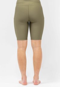 Achteraanzicht van een persoon die blootsvoets staat in olijfgroene, geribbelde, nauwsluitende shorts tot op de knie op een plain witte achtergrond.