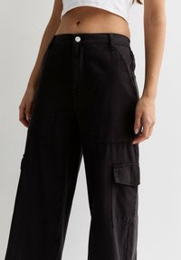 Svarta vida cargobyxor i hållbart tyg, med sidofickor och framfickor, knäppning med knapp och en slät yta.