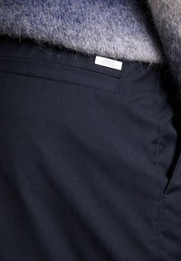 Pantalon bleu marine en tissu lisse, avec une poche avant et des coutures discrètes. Étiqueté avec une tag "Armani Exchange".