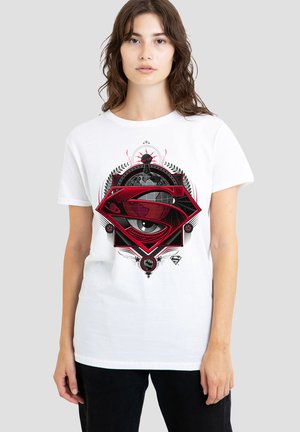 Woman wearing white shirt with a red and black Superman logo featuring a globe and a detailed eye design.