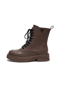Botas de tobillo de cuero marrón con cordones negros, puntera redonda y suela de plataforma texturizada. Cuenta con una asa en la parte posterior para facilitar el calzado.
