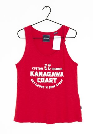 Camiseta sin mangas roja con escote redondo, hecha de tela suave. Presenta un texto blanco en negrita: "KANAGAWA COAST" con gráficos. Etiqueta colgante visible.