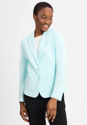 Mint green blazer with a tailored fit, two buttons, notched collar, and front pockets, worn over a white top and black pants.
