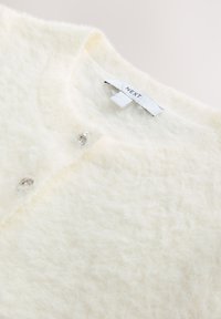 Cardigan bianco soffice realizzato in materiale morbido, con tre bottoni decorativi d'argento sul davanti e un'etichetta interna con marchio.