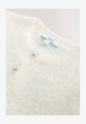 Bílý nadýchaný kardigan z měkkého materiálu, s třemi ozdobnými stříbrnými knoflíky na přední straně a vnitřní štítkem s označením.