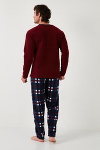 Bordový top s dlhým rukávom v kombinácii s kockovanými pyžamovými nohavicami v námorníckej modrej, červenej a bielej farbe. Pohodlná látka s mäkkou textúrou. Nohy sú bosé.