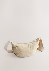 Bēšs auduma jostas maks ar gludu tekstūru, izliekta forma, regulējama siksna un rāvējslēdzēja aizdare. Smalka ribota raksta detaļa.