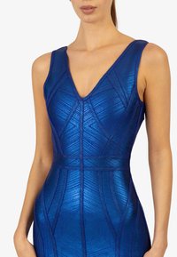Robe à col en V en tissu bleu métallique avec des motifs géométriques, présentant un design ajusté, des bretelles larges et une surface texturée.