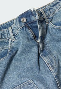Jean en denim bleu avec fermeture éclair métallique partiellement ouverte et bouton à la taille, montrant les poches avant et les passants de ceinture.
