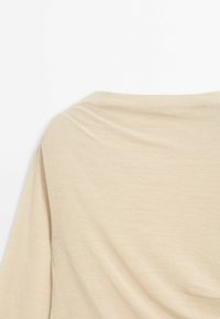 Beige knit top with a relaxed silhouette, featuring a draped neckline and soft texture. The fabric is lightweight and smooth.