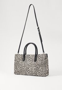Sac à main noir et blanc à pois avec deux poignées courtes et une bandoulière longue amovible. Matériau lisse avec une forme rectangulaire structurée.