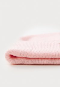 Μαλακό ροζ πλεκτό ύφασμα διπλωμένο προσεκτικά σε λευκή επιφάνεια, επιδεικνύοντας λεπτομερή ραφή και υφή.