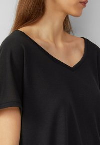 Haut noir à manches courtes et décolleté en V en tissu doux. Présente une coupe décontractée et une texture lisse. Design minimaliste sans motifs visibles.