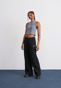Top corto blu e pantaloni neri larghi con cintura di regolazione. L'outfit presenta un piccolo logo bianco sui pantaloni. Scarpe con plateau nere.