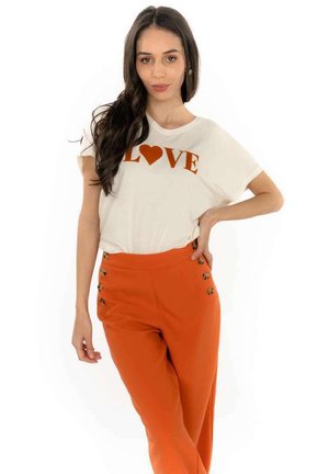 T-shirt blanc avec "LOVE" et un cœur en imprimé orange, associé à un pantalon taille haute orange avec des accents de boutons sur le côté.