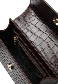 Interno di una borsa a mano in pelle di colore marrone scuro con effetto coccodrillo, dotata di tasca con zip e foderata in tessuto a motivo, con dettagli in metallo color oro.