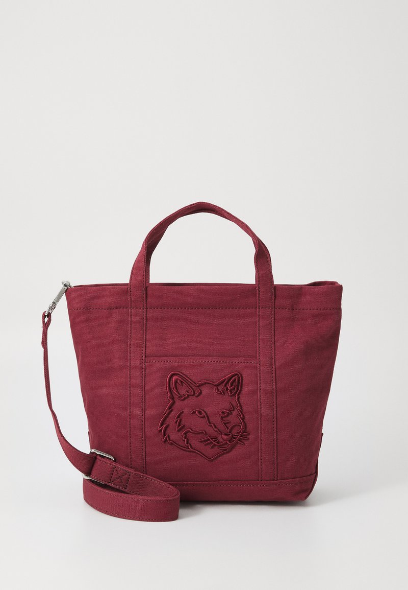 Burgundin värinen kassi, jossa on teksturoitu kangas, jossa on kohokuvioitu ketun pää -kuvio, kaksinkertaiset yläkahvat ja säädettävä olkahihna.