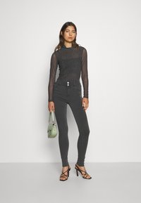 Top de malha preta de mangas longas com padrão de bolinhas, emparelhado com jeans skinny cinza escuro de cintura alta e saltos pretos com tiras, segurando uma bolsa verde-clara.