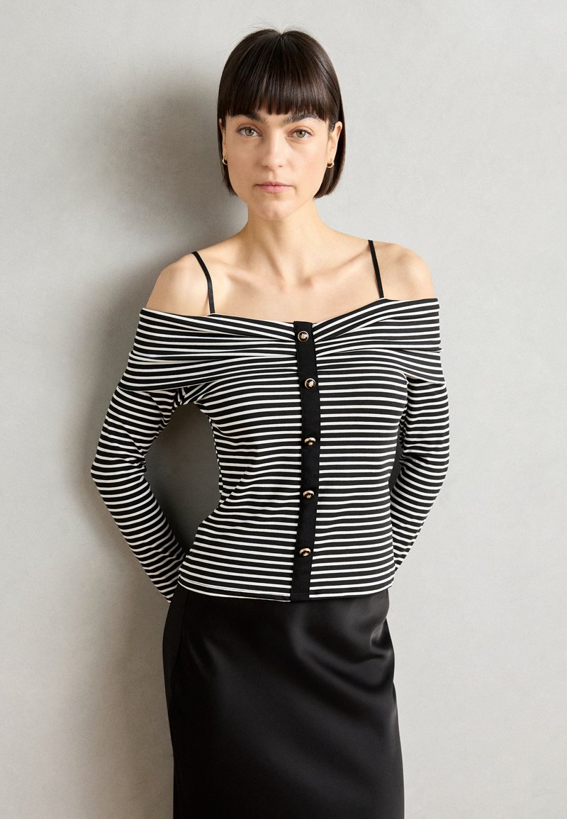 Haut off-shoulder à rayures noires et blanches avec un devant boutonné et des manches longues, associé à une jupe noire élégante. Texture de tissu lisse.