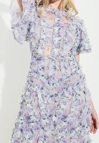 Lavendellila blommig klänning i genomskinlig tyg med volangdetaljer, som har korta ärmar och en lagerdesign.