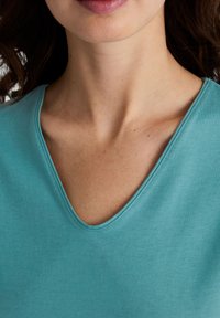 Turfkleurige v-hals top gemaakt van zachte stof, met een gladde textuur en een scherpe halslijn met subtiele stikseldetails.