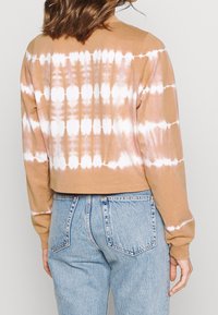 Béžová crop mikina s bílým batikovaným vzorem, dlouhými rukávy a měkkou texturou látky. Kombinováno s světle modrými džínami.