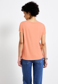 Košile s krátkým rukávem z jemné korálové tkaniny, s kulatým výstřihem a uvolněným střihem, v kombinaci se světle modrými džíny rovného střihu.