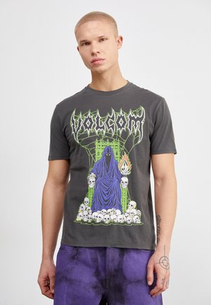 Camiseta de algodón gris con un gran gráfico de una figura encapuchada con calaveras, detalles en verde y texto "VOLCOM" en negrita. Mangas cortas.