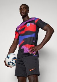 Nike football shirt features a purple, red, and black abstract pattern, with a logo; paired with black shorts showcasing an orange accent.