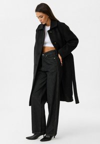 Zwarte wollen jas met een kraag en knopen, gecombineerd met hoge zwarte spijkerbroeken met contrasterende stiksels en zijzakken.