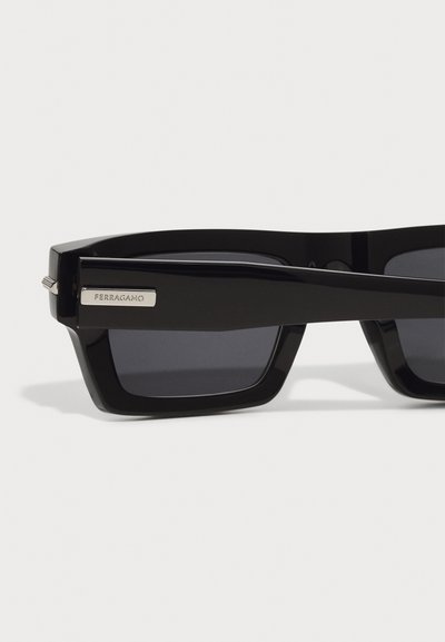 Ochelari de soare negri cu o ramă robustă, având lentile întunecate și un logo argintiu Ferragamo pe lateral. Finisaj neted cu design unghiular.