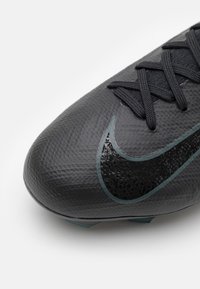 Acercamiento de una bota de fútbol negra texturizada con cordones negros y un emblema de swoosh de Nike negro y brillante en el lado frontal.