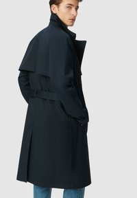 Cappotto trench navy con design doppiopetto, ampi rever, spacco posteriore e cintura regolabile. Realizzato in un tessuto leggero e liscio.