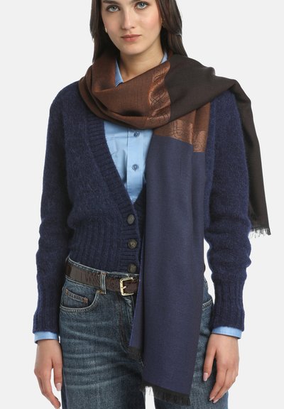 Mornarica pleteni kardigan s teksturiranim završetkom, uparen s smeškim i mornarskim šalom s uzorkom, plavom košuljom i tamnim trapericama. Remen s uzorkom krokodila.