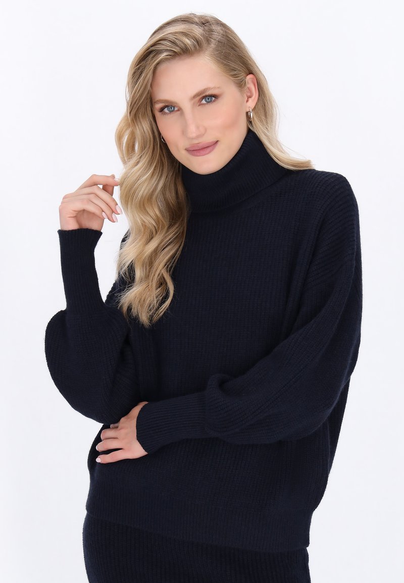 Maglione a collo alto blu navy con texture a coste, vestibilità oversize e maniche lunghe. Il materiale sembra morbido e caldo.