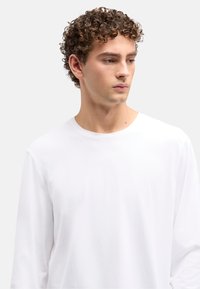 Hvid T-shirt med lange ærmer og rund hals, blød bomuldstekstur og afslappet pasform, med minimalistisk design uden synlige mønstre.