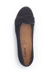 Schwarze Stoff-Ballettschuhe mit einem verknoteten Detail an der Zehe, sichtbaren Nähten und einer braunen gepolsterten Innensohle mit Perforationen. Markenname sichtbar.