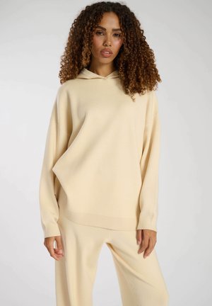 Crème-kleurige oversized hoodie met een trekkoord in de capuchon en geribde manchetten, gemaakt van een zachte, gestructureerde stof, gepresenteerd met een relaxte pasvorm.