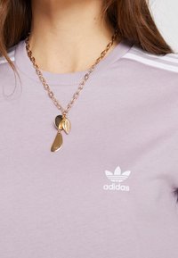 Lila kortärmad Adidas-tröja med vita tre-stripe detaljer och logotyp; matchad med ett guldhalsband med texturerade berlocker.