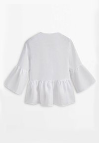 Blouse blanche avec manches longues évasées et bas patte d'oie froncé, vue de dos sur un fond uni.