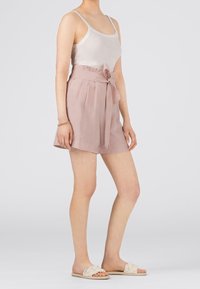 Vaaleanpunaiset pellavashortsit, joissa on solmittava vyö, laskostettu etuosa ja rento malli, yhdistetty valkoiseen tanktoppiin ja beigenvärisiin liukuvien sandaaleihin.